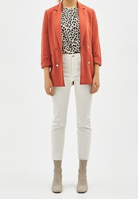 Červený blazer přes top s leopardím potiskem, doplněný bílými džínami a béžovými pletenými kotníkovými botami. Hladká látka, dobře padnoucí střih a kontrastující vzory.