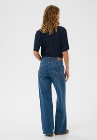 Kék, széles szárú, magas derekú farmernadrág részletes hátul zsebekkel és barna bőrpárnával az derékpánton. Texturált fekete ing.