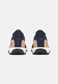 Zapatillas deportivas azules con acentos beige, tejido de malla, lengüeta en el talón y una entresuela blanca. Presenta un logotipo en el costado.