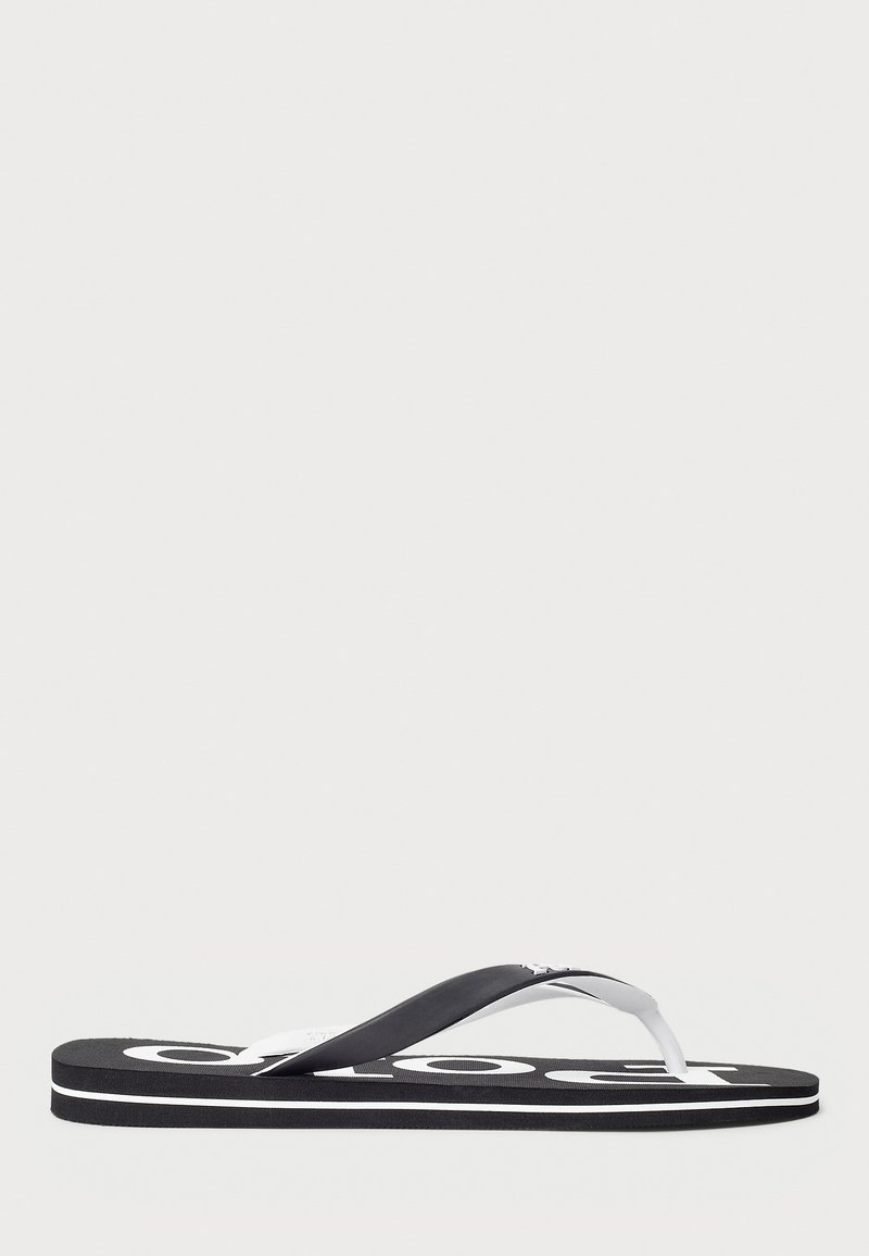 Czarne gumowe klapki z białymi akcentami, z teksturowaną podeszwą i szerokim paskiem między palcami. Wyróżniające się logo nadrukowane na podeszwie.