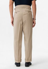 Beige broek met een getailleerde pasvorm, omgeslagen zoom en twee achterzakken met messing knopen. Gemaakt van een soepele, lichte stof.