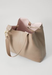 Borsa tote in pelle beige con una texture morbida, ampia apertura, dettagli in metallo dorato e interno rosa chiaro. Include una tracolla regolabile.