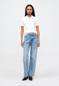 Fehér, textúrált, rövid ujjú póló, világoskék, kopott széles szárú farmernadrággal és fekete bokacsizmával párosítva.