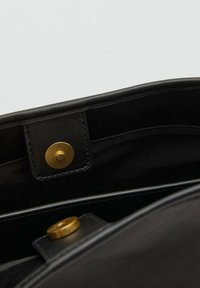 Interiorul unei genți de mână din piele neagră, cu un închizător prin buton circular de aur și buzunare simple de organizare. Textură netedă cu un design minimalist.