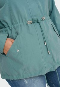 Šviesiai mėlynas švarkas su suspaustu liemeniu, raišteliu ir šoninėmis kišenėmis. Pagamintas iš lygaus audinio su minimalistiniu dizainu.