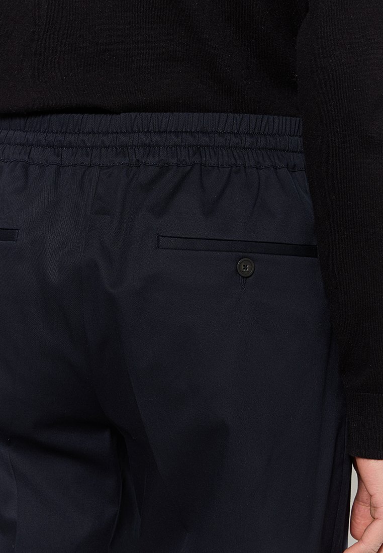 Marineblau Hosen mit elastischem Bund, seitlichen Taschen und einem einzigen Knopfdetail. Der Stoff wirkt glatt und leicht.