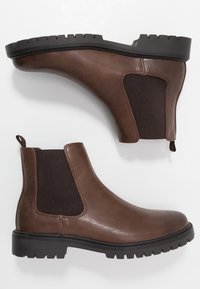 Botas Chelsea de cuero marrón con paneles laterales elásticos, suelas texturizadas y una lengüeta para facilitar el uso. Tacón plano, diseño elegante.