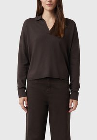 Ciemnobrązowy sweter z dekoltem w kształcie litery V i kołnierzykiem, luźny krój, długie rękawy i ściągacze na mankietach. W zestawie z pasującymi ciemnymi spodniami.
