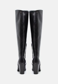 Botas de cuero negro hasta la rodilla con un acabado brillante, tacones de bloque resistentes, cremalleras laterales y detalles de costura sutiles.