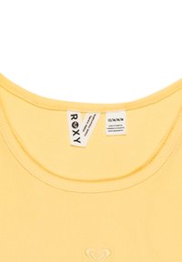 Gul ribbad bomullstanktop med rund halsringning och en liten broderad logotyp i mitten. Skötselråd är synligt.