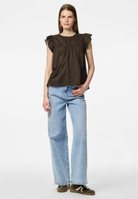 Top in cotone marrone con maniche arricciate e dettagli in pizzo, abbinato a jeans a gamba larga azzurri chiari e sneakers scure con strisce chiare.