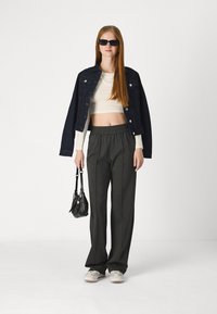 Veste en denim, haut blanc court, pantalon large gris et baskets grises. Sac à main noir avec accent en chaîne. Cheveux longs et raides et lunettes de soleil.