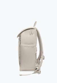 Sac à dos beige au design structuré, doté d'une poche avant, de fermetures éclair et de bretelles réglables. Texture lisse et style minimaliste.