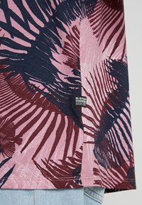 Koszulka T-shirt z krótkim rękawem w kolorze różowym i granatowym z wzorem liści. Materiał ma miękką teksturę. Zawiera metkę G-Star Originals na dolnym końcu.