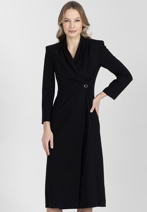 Czarna sukienka z dopasowanym górą, długimi rękawami i dekoltem w kształcie litery V. Posiada pojedyncze zapięcie na guzik oraz plisowaną spódnicę sięgającą do połowy łydki.
