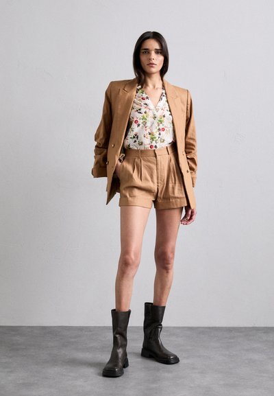 Beige linblazer over en hvit blomstrete skjorte, sammen med beige høyt liv bukser og svarte lær ankelstøvler. Enkel og skreddersydd design.