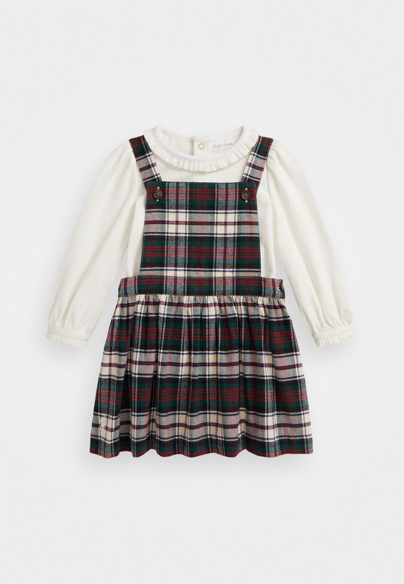 Vestido xadrez com uma camisa de manga longa branca por baixo. O vestido apresenta cores verde, vermelha e creme, com um colarinho franzido e alças com botões.