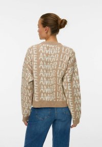 Femme avec les cheveux en chignon portant un pull beige avec un texte répété "AMOR LOVE" en blanc et un jean bleu, dos à la caméra.