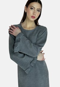 Vestido gris texturizado con mangas largas y rizadas; presenta un escote redondo y un corte holgado, destacando la superficie suave de la tela.