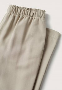 Pantalon beige à taille élastique, plié soigneusement sur une surface blanche, montrant un tissu lisse et une couture simple.
