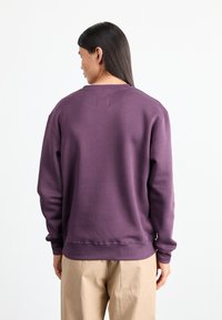 Purple sweatshirt with a classic crew neckline, ribbed cuffs and hem, and a small tag detail on the back. Casual fit, smooth texture.