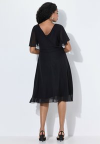 Robe noire avec des manches courtes et légères, un dos en V et une silhouette fluide. Tissu doux avec une longueur au genou et des détails en dentelle subtils.