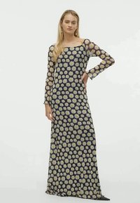 Vestido longo e transparente preto com um padrão floral de margaridas brancas e amarelas. Possui mangas longas e um decote quadrado. Tecido fluido.