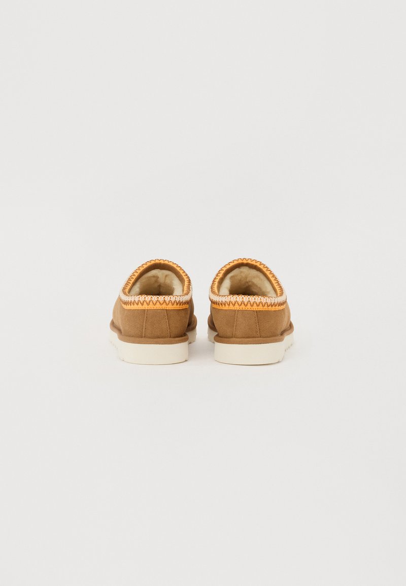 Le scarpe slip-on in suede marrone presentano un morbido rivestimento interno e cuciture arancioni lungo il bordo superiore, con una suola in gomma bianca.