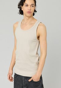 Débardeur beige avec texture côtelée, col rond classique et larges bretelles, assorti à un short gris foncé à coupe décontractée.