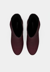 Μποτάκια μπορντό με ομαλή υφή, στρογγυλεμένη μύτη και μινιμαλιστικό σχέδιο. Διαθέτουν χαμηλή κοπή στον αστράγαλο και διακριτική σήμανση εσωτερικά.