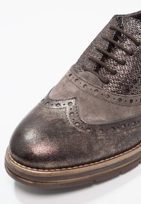 Chaussure brogue pour homme en cuir gris métallique, tige en mesh texturé et perforations décoratives. Équipée d'une semelle marron robuste.