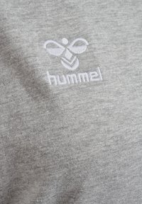 Pelēks sporta krekls ar mīkstu, teksturētu audumu. Iekļauj baltu izšuvumu ar bišu logotipu un zīmola nosaukumu "hummel" zem tā.