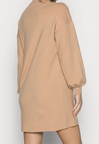 Beige pletené šaty s dlouhými balónovými rukávy a volným střihem, s kulatým výstřihem a bočními rozparky pro snadný pohyb.