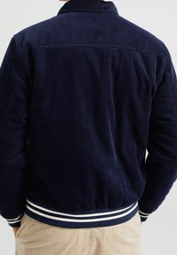 Marinblå kordjacka med ribbad textur, krage och randig elastisk midja. Har en klassisk passform och detalj vid ryggen.