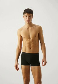 Melnās kokvilnas boksera bikses ar mīkstu jostu, ar pieguļošu dizainu un gludu tekstūru. Modelis stāv uz vienkārša fona.