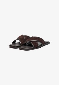 Brune flettede sandaler med flad sål, der har teksturerede stropper og et elegant design. Accenterne er glatte og ensartede i farven.