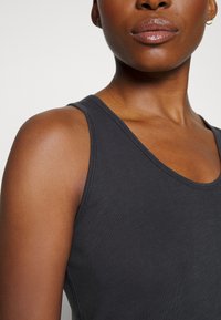 Camisola preta sem mangas, feita de tecido suave, com um decote redondo e detalhes de costura mínimos, ajustada nos ombros.