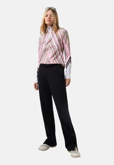 Multi-colored, striped long-sleeve top with high collar, paired with black pants; features a relaxed fit and soft texture. Sporty shoes complete the look.