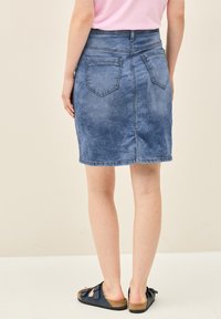 Denimhame vaaleansinisessä pesussa, polvimittainen, tiukalla vyötäröllä, kahdella takataskulla ja hienovaraisella kulumisella. Yhdistetty tummiin sandaaleihin.