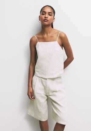 Top corto in lino beige con sottili spalline a spaghetto abbinato a pantaloni corti a vita alta coordinati. Taglio semplice e rilassato con una leggera lucentezza.