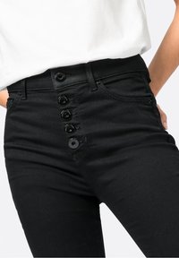 Jeans negros de talle alto con cierre frontal de cinco botones negros, corte recto y diseño clásico de bolsillos.