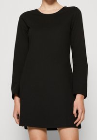 Svart långärmad klänning i ett slätt material med rundad halsringning, en avslappnad passform och en fåll som slutar ovanför knäet.
