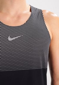 Débardeur de sport noir avec un motif triangulaire blanc géométrique, col rond et petit logo argenté Nike sur la poitrine.