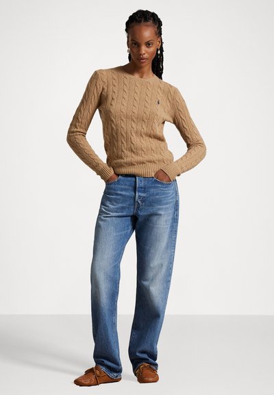 Pull en maille torsadée beige, jean droit bleu, et chaussures mocassins marron. Design simple avec de la texture dans le tissage du pull.