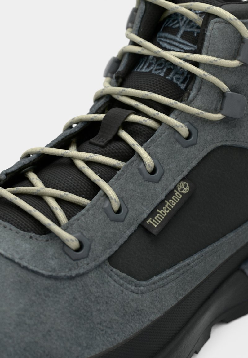Gray hiking boot featuring a suede upper, black accents, and cream laces. Notable logo detail and textured rubber sole.