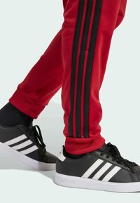 Melnas sporta kurpes ar baltām svītrām, apvienotas ar sarkaniem sporta biksēm ar melnām sānu svītrām. Gluda virsma ar ribotām piedurknēm.