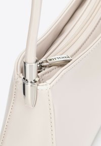 Sac à main beige clair en matériau synthétique lisse, avec une fermeture éclair et des accessoires en argent. Le nom de la marque "WITTCHEN" est visible sur la tirette de la fermeture éclair.