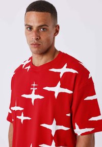 Rode korte mouw t-shirt met een gedurfde witte kruispatroon. Zachte stof met een ronde hals en een klein logo in het midden.