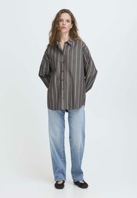 Brun og blå stribet oversized skjorte med knaplukning, lange ærmer og afslappet pasform, parret med lyseblå lige ben jeans.