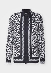 Μαύρο και λευκό μακρυμάνικο πουκάμισο με έντονα σχέδια κειμένου και λεπτομέρειες από αλυσίδα, με κλασικό γιακά και κλείσιμο με κουμπί.